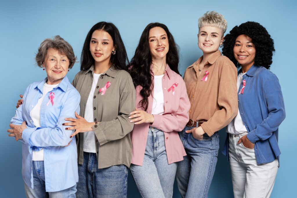 Group of women of different ages and ethnicities standing together, wearing pink ribbons, symbolizing unity in breast cancer awareness